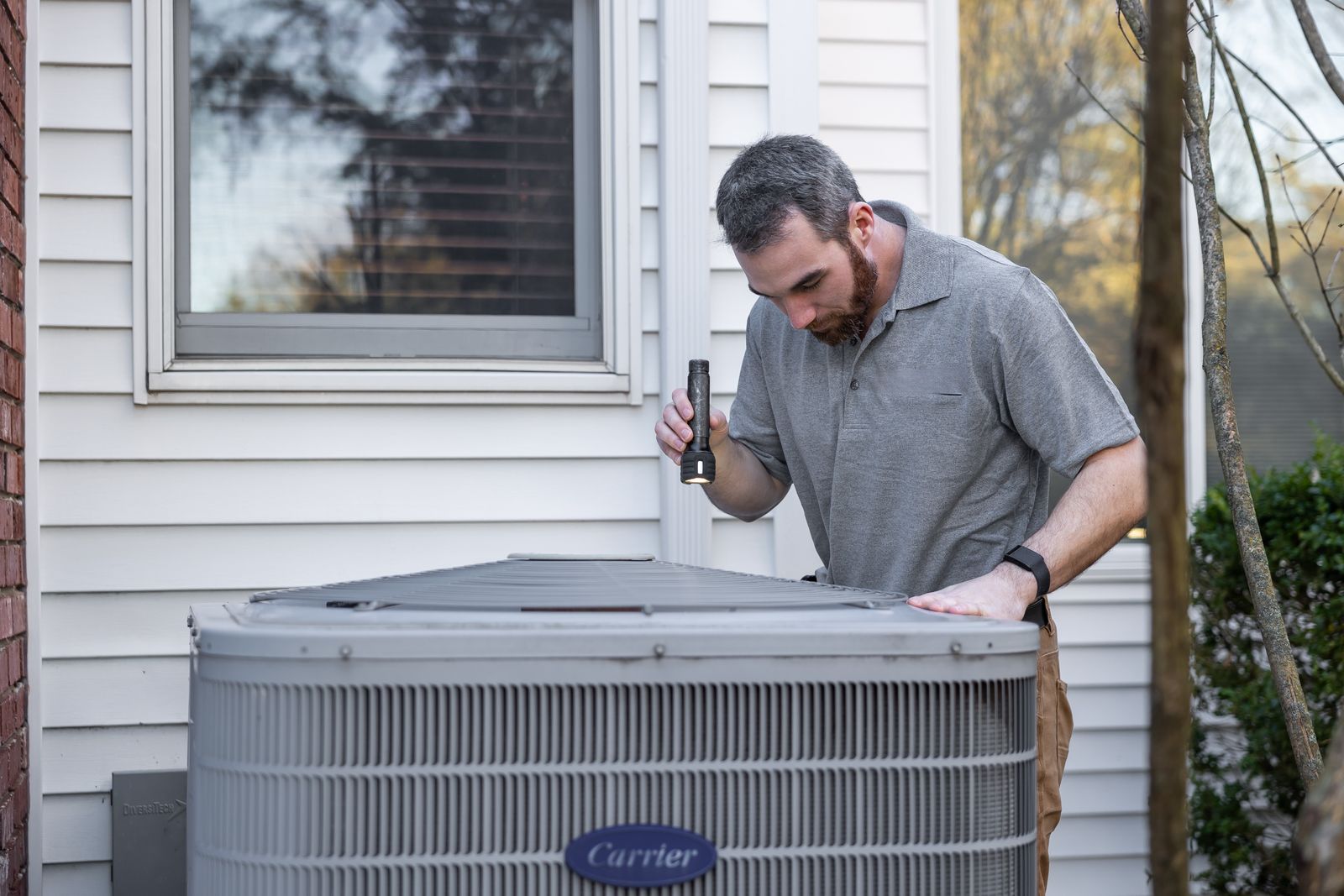 HVAC technician inspecting an outdoor air conditioning unit beside a home during a maintenance visit