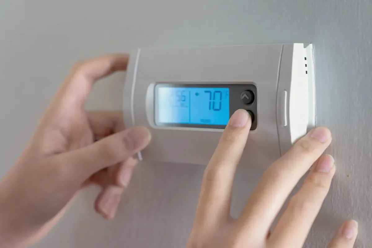 Hands adjusting a digital wall thermostat